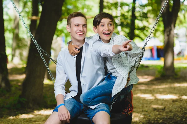 Ragazzi sorridenti che si divertono al parco giochi. Bambini che giocano all'aperto in estate. Adolescenti che cavalcano su un'altalena fuori — Foto Stock