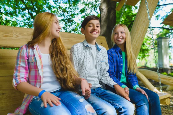 Ragazze e ragazzi sorridenti che si divertono al parco giochi. Bambini che giocano all'aperto in estate. Adolescenti su un'altalena . — Foto Stock