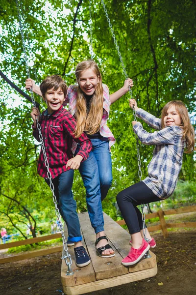 Senyum anak-anak bersenang-senang di taman bermain. Anak-anak bermain di luar ruangan di musim panas. Remaja naik di ayunan di luar — Stok Foto