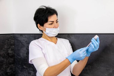 Sürecten önce, güzellik salonunda beyaz önlüklü, şırıngalı ve eldivenli bir kız doktor.