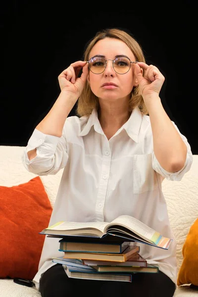 戴眼镜、身穿白衬衫的老师坐在沙发上，拿着书本，全神贯注地向前看 — 图库照片