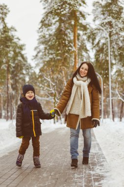 Happy family in winter clothing. Smiling mother and son walk at the park