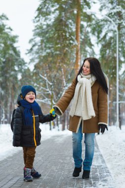 Happy family in winter clothing. Smiling mother and son walk at the park