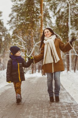 Happy family in winter clothing. Smiling mother and son walk at the park