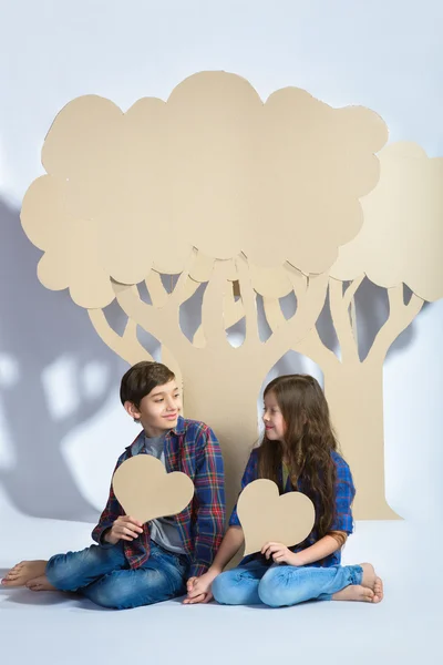Chłopiec i dziewczynka zachować serce siedzieć pod drzewem karton. Koncepcja miłości — Zdjęcie stockowe