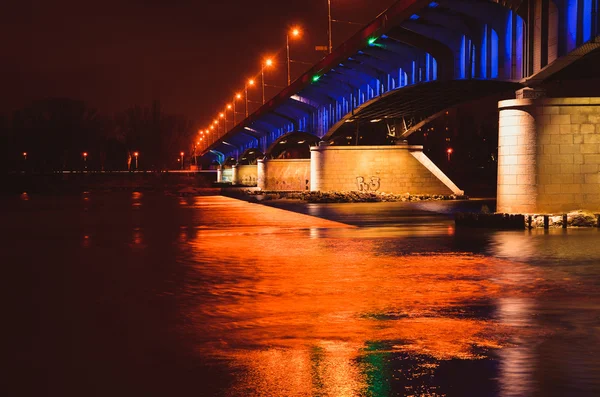 Slasko-dabrowski Brücke beleuchtet in der Abenddämmerung mit Reflexionen auf Wasser und Pier auf dem Weichsel Fluss in Warschau, Polen. — Stockfoto