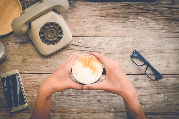 Mãos de homem segurando xícara de café no fundo de madeira, vista superior , — Fotografia de Stock