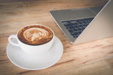 Vintage filtre etkisi ile ahşap masada Kahve fincanı ve dizüstü bilgisayar