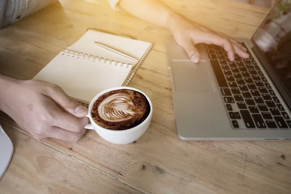 Homem de negócios segurando uma xícara de café e usando laptop — Fotografia de Stock