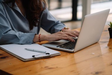 Öğrenci kız ellerinin, evdeki bir masada oturup dizüstü bilgisayardaki notları karşılaştırması..