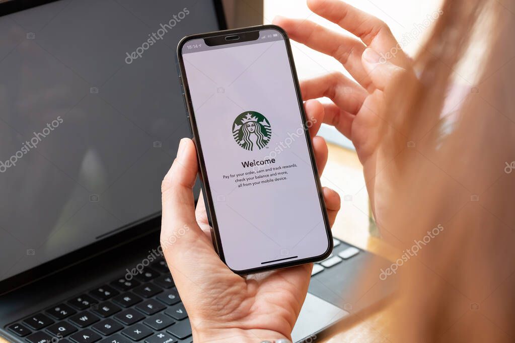 Chiang Mai, Thailand : Mar 7 2021 : A woman holds iPhone 12 showing Starbucks logo on screen in Starbucks coffee shop