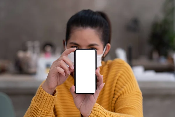 Макет изображения красивой женщины носить маску, держа мобильный телефон с чистым белым экраном. — стоковое фото