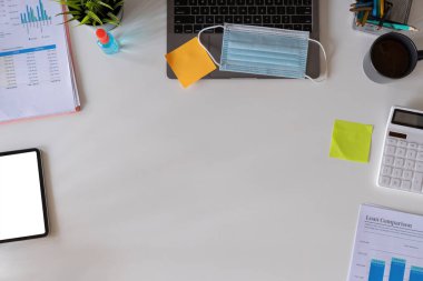 İş yerinin tıbbi yüz maskesi ve el dezenfektanı. Düz dizüstü bilgisayarı ve kopyalama alanı olan beyaz çalışma alanı arkaplanı vardı. Üst görünüm