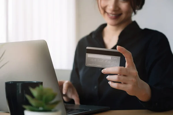 若い女性はクレジットカードを保持し、自宅でラップトップコンピュータを使用しています。オンラインショッピング、電子商取引、インターネットバンキング、お金を使う. — ストック写真
