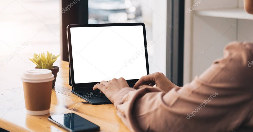 Cropped shot of young professional businesswoman typing on blank screen tablet and office supplies in simple workspace.