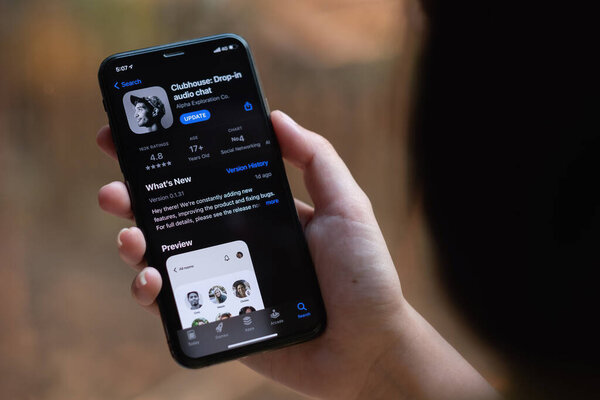 CHIANG MAI, THAILAND, 13 MAR 2021 : Woman in Wired Headphones holding Smartphone with Clubhouse drop in audio chat application on screen. New social network launched in 2020 by Alpha Exploration Co
