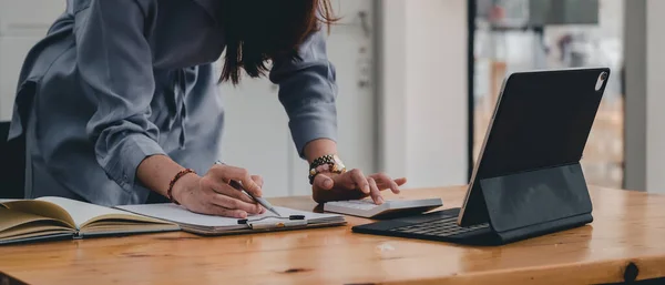 Affärskvinna eller revisor som noterar och arbetar med miniräknare och bärbar dator för att beräkna affärsdata under anteckna på anteckningsblock, bokföringsdokument på kontoret — Stockfoto