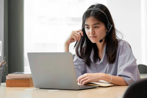 젊은 아시아인 소녀나 학생들에게 노트북을 들고 책 학습을 하는 것을 집중적으로 보게 했습니다. 진지 한 여성은 컴퓨터로 연구를 하거나 컴퓨터로 공부를 하거나 온라인으로 시험 준비를 합니다.. — 스톡 사진