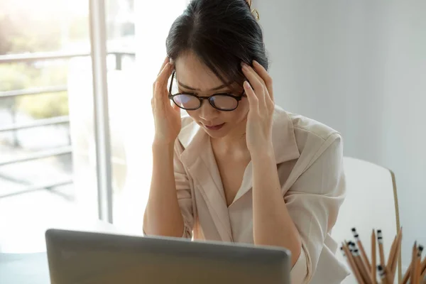 Уставшая азиатская деловая женщина с головной болью от работы ноутбука чувствует головную боль в офисе, чувствует себя больным на работе — стоковое фото