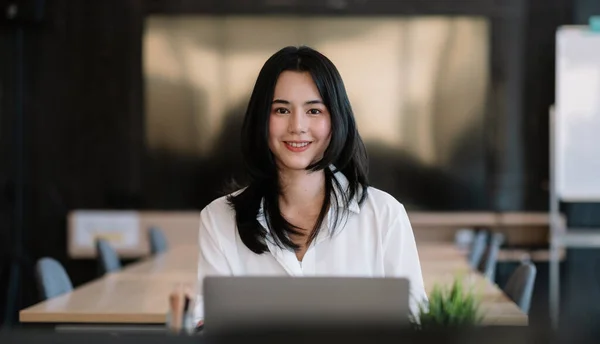 Uśmiechnięta młoda azjatycka bizneswoman siedząca na swoim miejscu pracy w biurze. Młoda kobieta pracująca na laptopie w biurze — Zdjęcie stockowe
