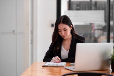 sian young woman seriously working on computer laptop and checking data report at home office