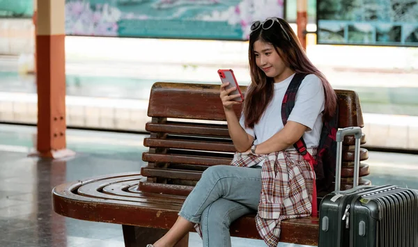 Asyalı kadın tren istasyonunda treni bekliyor. seyahat konsepti. Gezgin çevrimiçi gezi planlaması için akıllı telefon kullanıyor — Stok fotoğraf
