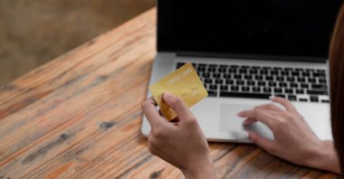Kredi kartı tutan ve dizüstü bilgisayar kullanan eller. Kahve dükkanından online alışveriş.