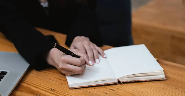De cerca la mano de la mano de la mujer que sostiene la pluma tomando nota y trabajando con el ordenador portátil en la oficina de la mesa — Foto de Stock