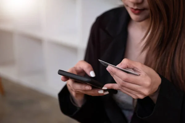 Fechar mulher segurando telefone e cartão de crédito no café. Uma bela menina asiática pagar por compras com um cartão e telefone — Fotografia de Stock