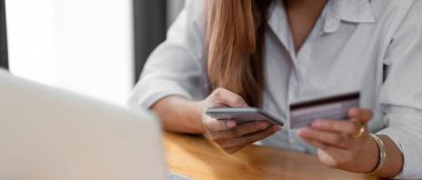 Close up asian woman using smartphone and credit card for online shopping at home with copy space. E-payment technology, shopaholic lifestyle, or mobile phone financial application concept.