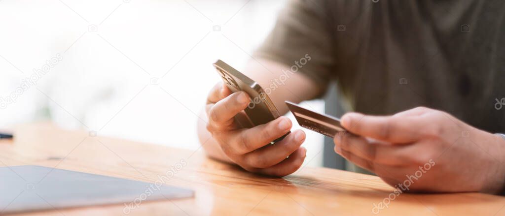 Online payment, Mans hands holding a credit card and using smart phone for online shopping at coffee cafe shop