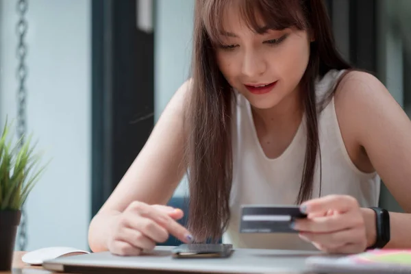 Портрет молодої азіатської жінки, яка посміхається і тримає кредитну картку і використовує смартфон для покупки в Інтернеті вдома, концепція оплати онлайн — стокове фото