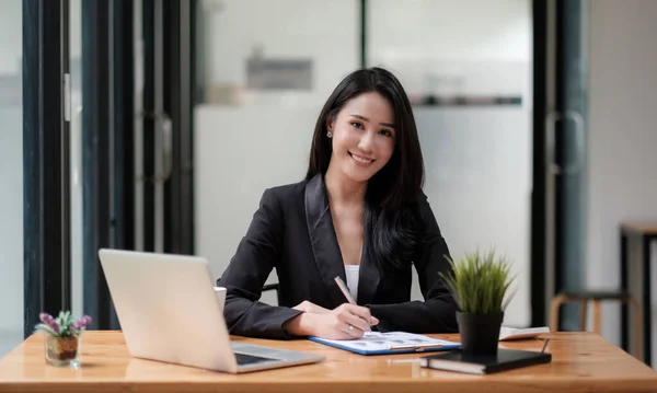Genç Asyalı iş kadını portresi. Güzel büyüleyici gülümseme. Ofiste iş mali raporu ve dizüstü bilgisayarla çalışırken. — Stok fotoğraf
