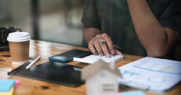 Man calculating financial chart for investment to buying property with house model. Male using calculator for house loan