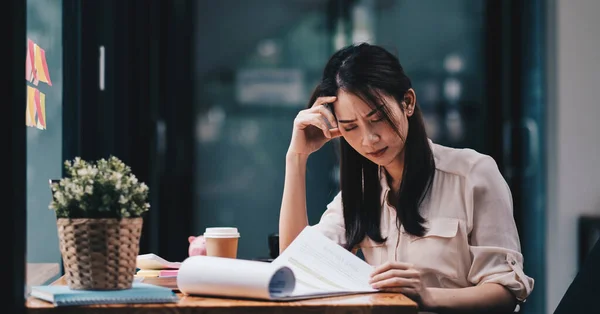 Unavená mladá Asiatka pociťuje bolest hlavy z pracovního problému. Stres žena trpí bolestí hlavy špatný zrak problém sedět na pracovišti. — Stock fotografie