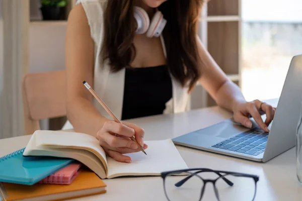 Молодая деловая женщина сидит за столом и делает заметки в notebook.On стол ноутбук, смартфон и чашку кофе. Обучение студентов онлайн. — стоковое фото
