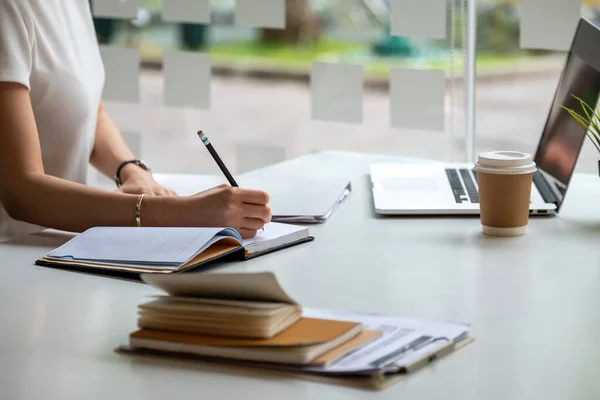 Nahaufnahme Asiatin macht Notizen auf ihrem Notizbuch für Online-Kurse, Ideen studieren und Notizen. Bildung online mit Laptop-Computer — Stockfoto