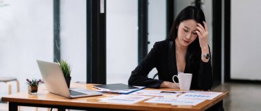 Genç Asyalı iş kadını iş yerinde oturuyor ve pazarlama raporuyla çalışıyor. Dizüstü bilgisayar kullanan ünlü.