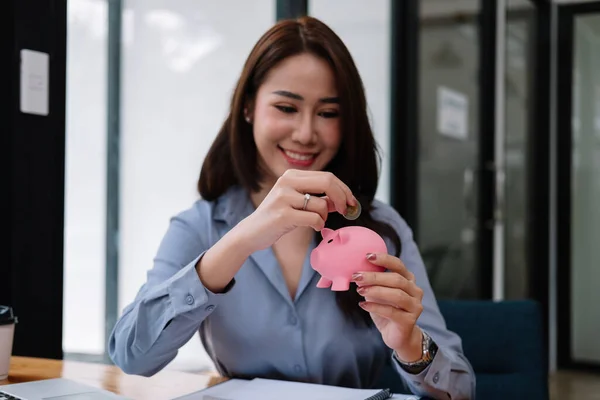 Крупним планом красуня азіатська жінка кладе грошову монету в рожевий скарбничку для економії грошового багатства та фінансової концепції — стокове фото