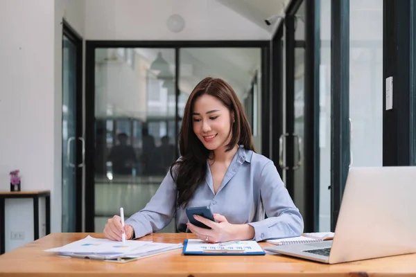 Negócios mulher asiática usando smartphone para fazer matemática finanças em mesa de madeira no escritório, imposto, contabilidade, conceito financeiro — Fotografia de Stock