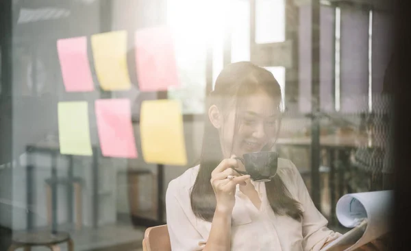 Shot van aziatische zakenvrouw werken tijdens het drinken van offee met financieel document op haar kantoor — Stockfoto