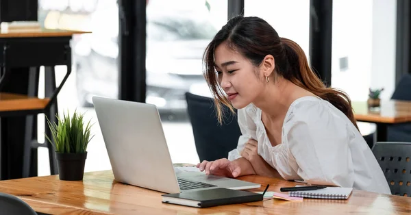 Sonriente chica asiática estudiante usando ordenador portátil estudio en línea con el profesor, feliz joven mujer aprender idioma escuchar conferencia ver webinar escribir notas mirar portátil sentarse en la cafetería, la educación a distancia. — Foto de Stock