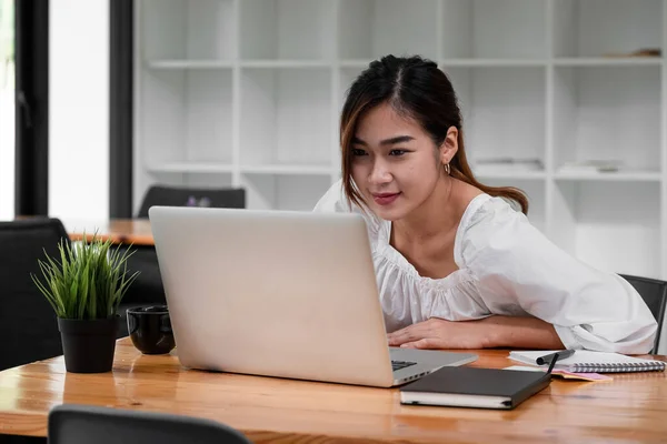 Sonriente chica asiática estudiante usando ordenador portátil estudio en línea con el profesor, feliz joven mujer aprender idioma escuchar conferencia ver webinar escribir notas mirar portátil sentarse en la cafetería, la educación a distancia. — Foto de Stock