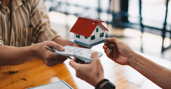 Närbild av händer ger hus modellen till andra händer med pengar. begreppet fastigheter och affären. — Stockfoto