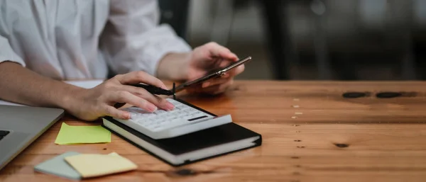 Närbild hand revisor eller bokhållare med hjälp av miniräknare och mobiltelefon, beräkna finansiella kostnader på hemmakontoret — Stockfoto