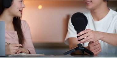 İki genç yetişkin canlı bir podcast etkileşimi içinde, takım çalışması ve yaratıcılığı gündelik bir ortamda sergiliyorlar..