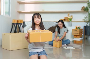 Bir kız gururla bir kutu tutarken annesi yeni evlerini düzenliyor, aile çalışmalarını ve heyecanı sergiliyor..