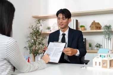 Bir emlakçı, bir emlak satın alma veya satma sürecini kolaylaştıran bir sözleşmeyi müşteriye gösterir.