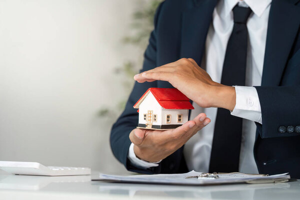 A real estate agent holds a model house, emphasizing its value while discussing property details with a client.