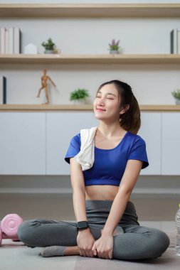 Bir kadın omuzunda havluyla bacak bacak üstüne atarak oturur, antrenmandan sonra gülümser, rahatlık ve rahatlığı somutlaştırır..